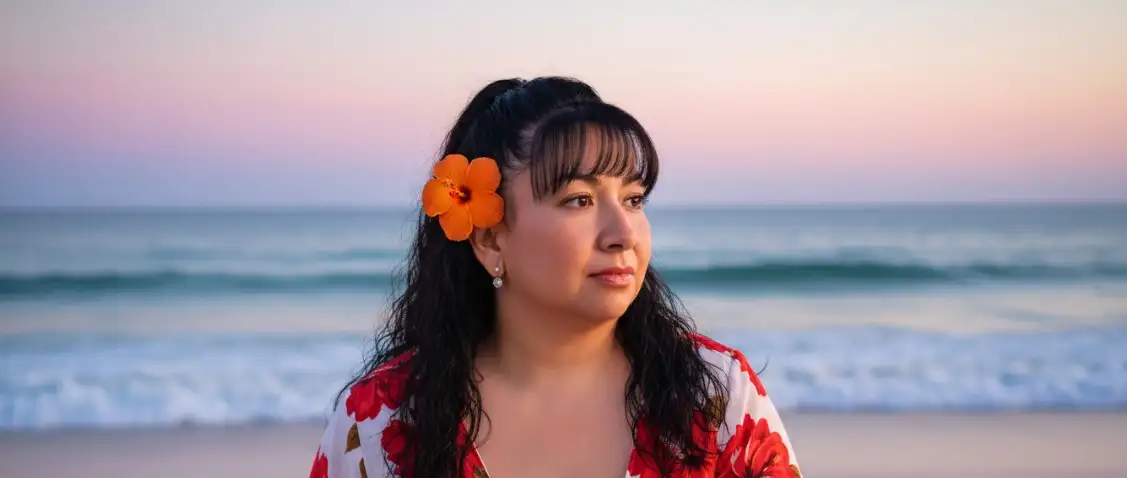 Crea un retrato ultrarrealista al aire libre de una mujer Mantén el rostro sin cambiarlo y sin modificarlo, sentada con gracia en la playa al atardecer. Luce un vaporoso vestido blanco con llamativos estampados florales rojos. Una flor tropical de color naranja brillante adorna su oreja, añadiendo un toque de elegancia. Su cabello cae naturalmente sobre sus hombros, complementando el ambiente romántico. Las olas del mar y el horizonte resplandecen suavemente bajo un cielo vespertino colorido con tonos rosas, morados y azules. La iluminación es suave y cinematográfica, resaltando su rostro y su vestido, a la vez que mantiene un fondo onírico. Fotografía de moda fotorrealista y profesional, resolución 4K.